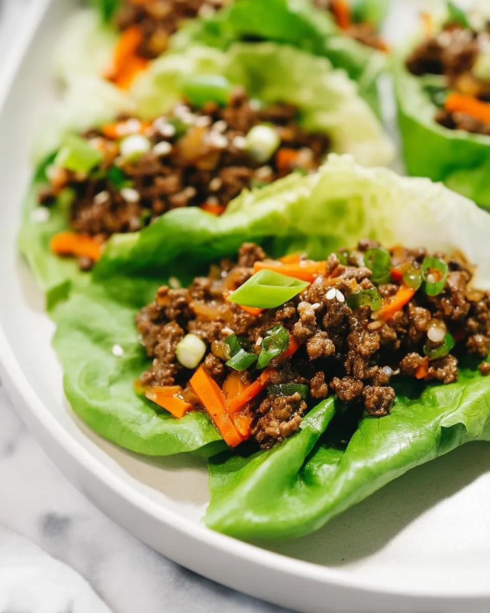 Asian Ground Beef Lettuce Wraps served on crisp romaine leaves with shredded carrots, green onions, and a drizzle of soy-ginger sauce.