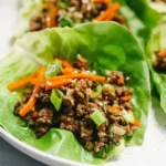 Asian Ground Beef Lettuce Wraps served on crisp romaine leaves with shredded carrots, green onions, and a drizzle of soy-ginger sauce.