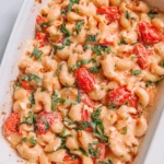 Baked feta pasta with roasted cherry tomatoes, creamy sauce, and fresh basil in a white serving dish.