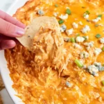 Close-up of creamy Buffalo Chicken Dip topped with melted cheese, served hot with tortilla chips on the side.