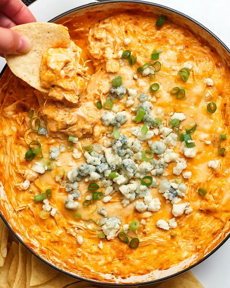 Close-up of creamy Buffalo Chicken Dip topped with melted cheese, served hot with tortilla chips on the side.