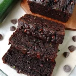 A thick slice of moist chocolate zucchini bread with rich chocolate chips, set on a rustic wooden board.