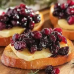 Crispy crostini topped with balsamic roasted cranberries and creamy brie on a serving board. Caption: Crispy Crostini with Balsamic Roasted Cranberries and Creamy Brie – a festive and flavorful appetizer.