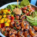 Colorful Mediterranean shrimp and avocado bowls topped with fresh mango salsa and drizzled with zesty lime-chili sauce, served in a white bowl.