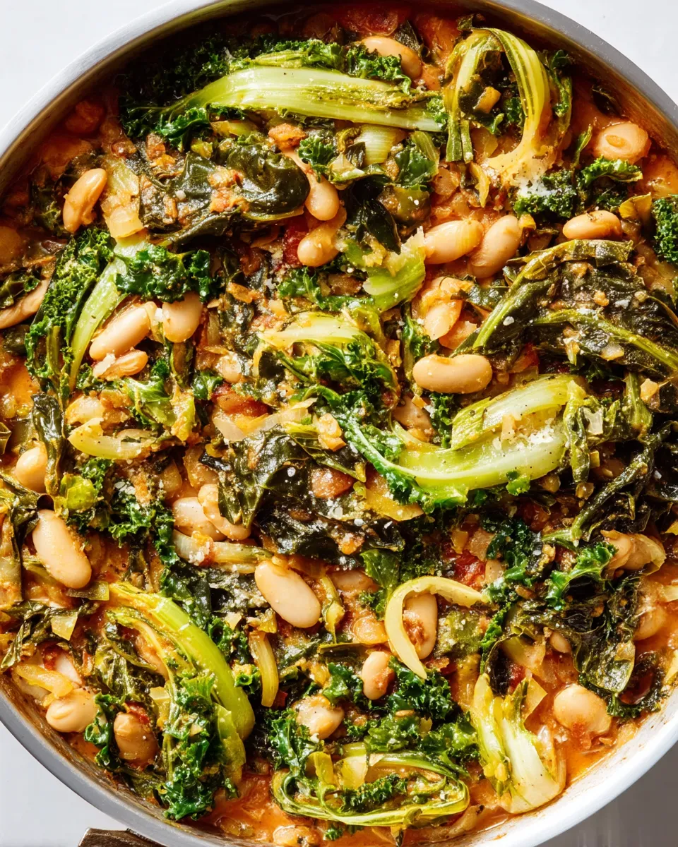 A rustic bowl of Mediterranean white beans and sautéed greens garnished with lemon wedges and fresh herbs.