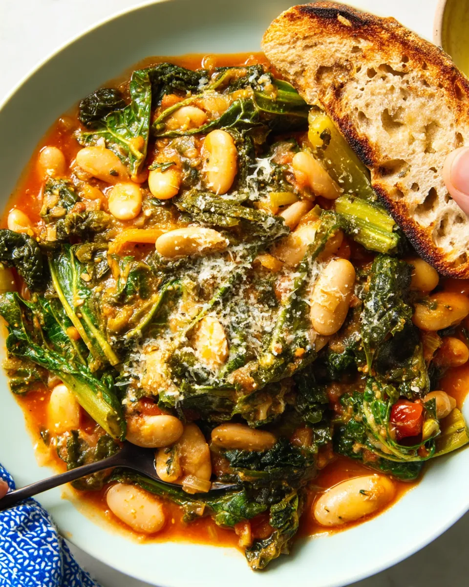 A rustic bowl of Mediterranean white beans and sautéed greens garnished with lemon wedges and fresh herbs.