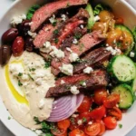 Mediterranean steak bowl filled with grilled steak slices, fresh vegetables, herbed couscous, and creamy tzatziki sauce in a rustic ceramic bowl.