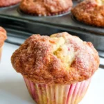 Freshly baked rhubarb muffins with Greek yogurt, showing golden-brown tops with cinnamon sugar crust and pink rhubarb pieces visible in the moist muffin crumb.