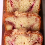 Freshly baked rhubarb bread loaf sliced and served on a wooden board, showing moist texture and pink rhubarb specks.