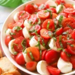 Fresh Caprese salad with ripe tomatoes, mozzarella slices, fresh basil, and a drizzle of balsamic glaze on a white plate.