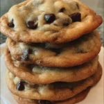 A stack of golden brown homemade chocolate chip cookies with gooey melted chocolate and crisp edges on a cooling rack.