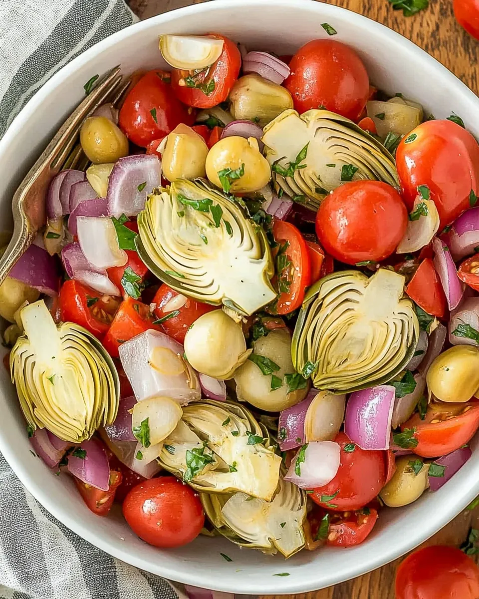 Colorful Tuscan Artichoke Tomato Salad with fresh basil, cherry tomatoes, and marinated artichokes on a white plate.