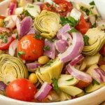 Colorful Tuscan Artichoke Tomato Salad with fresh basil, cherry tomatoes, and marinated artichokes on a white plate.