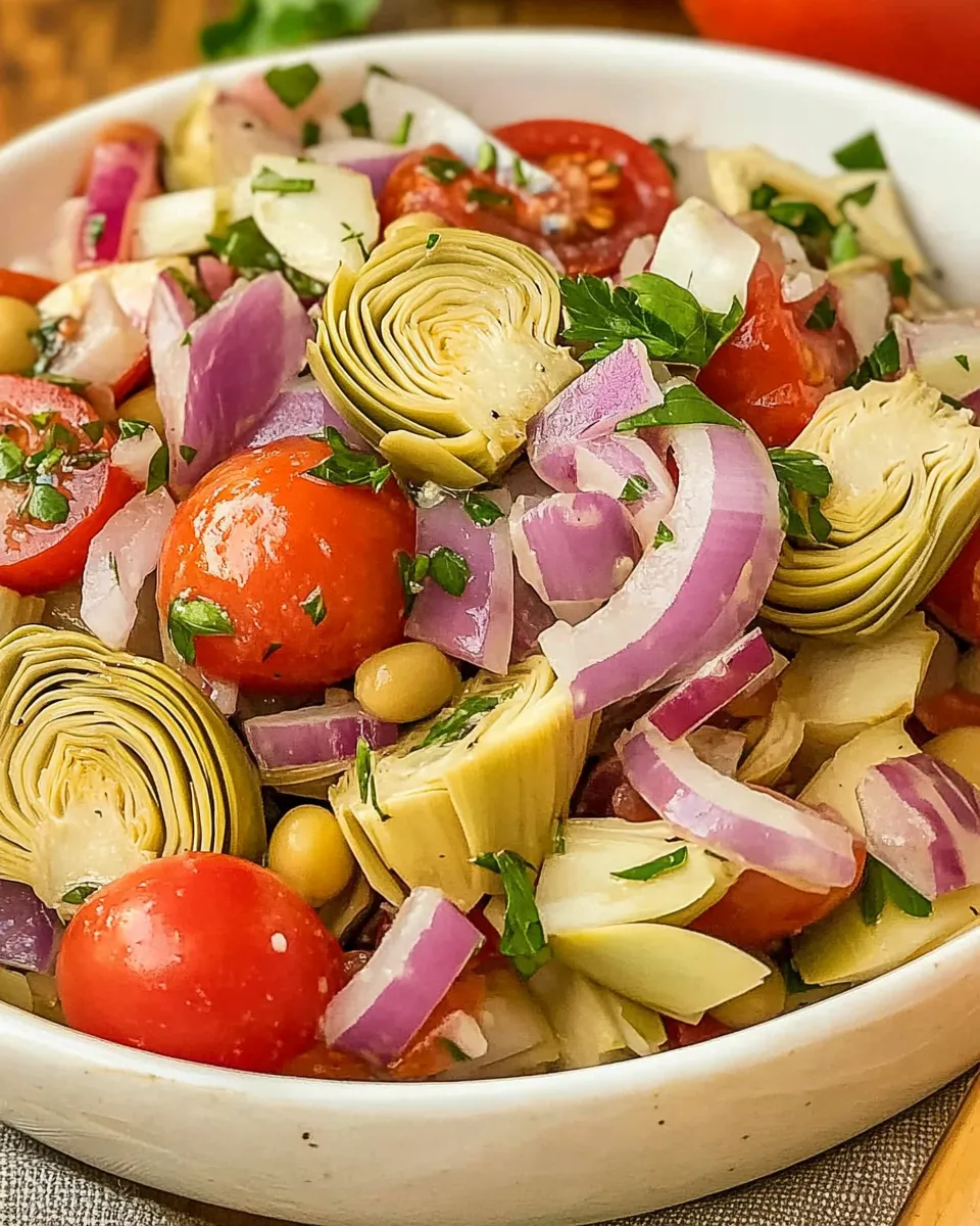 Colorful Tuscan Artichoke Tomato Salad with fresh basil, cherry tomatoes, and marinated artichokes on a white plate.