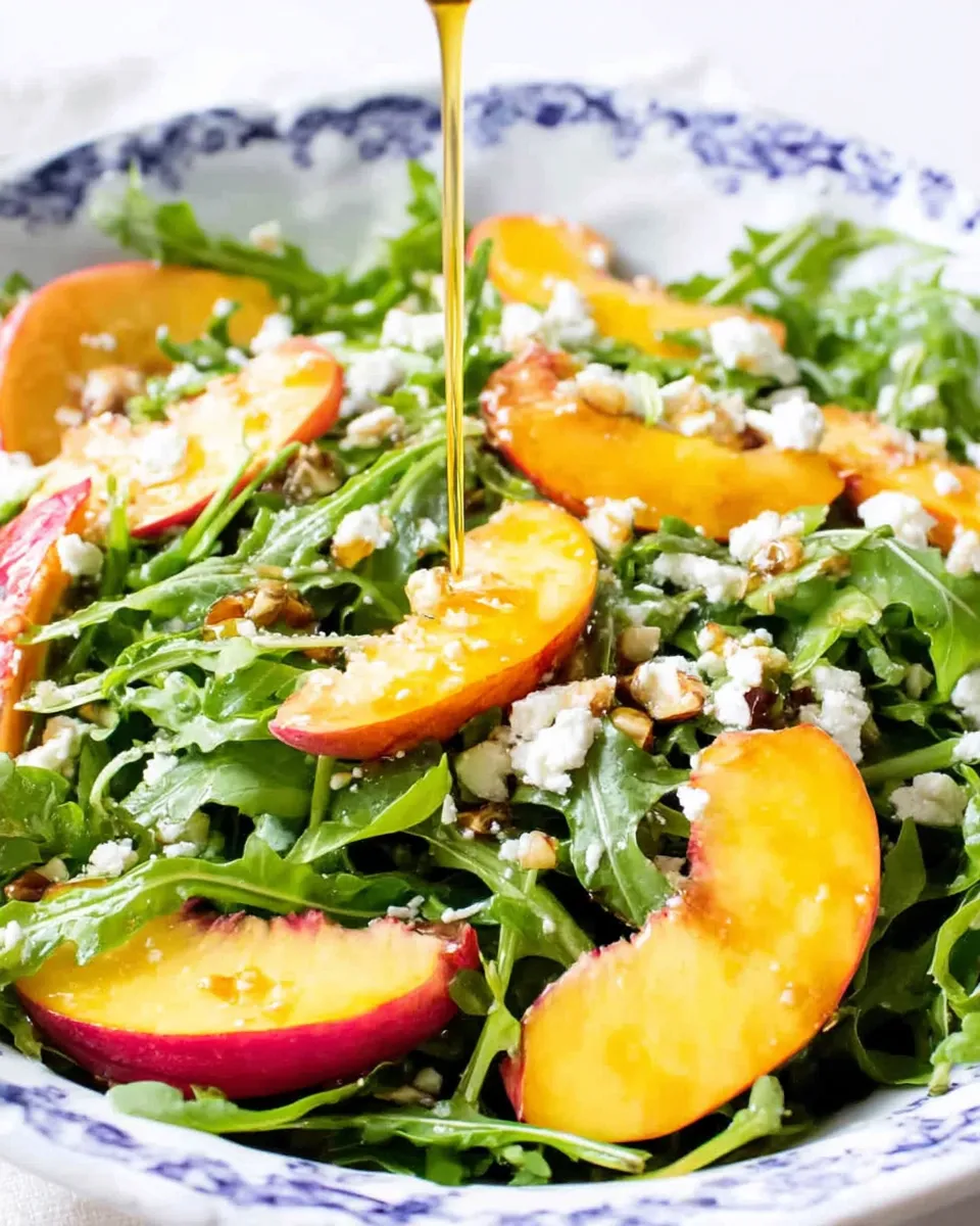 Fresh arugula nectarine salad with crumbled feta, toasted almonds, and a drizzle of balsamic vinaigrette served on a white plate.