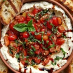 A bowl of fresh bruschetta dip made with chopped tomatoes, garlic, basil, and balsamic glaze, served with crispy toasted baguette slices on the side.