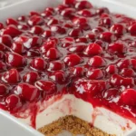 A layered Cherry Delight dessert with a buttery graham cracker crust, fluffy cream cheese filling, and glossy cherry pie topping, chilled and served in a square slice.