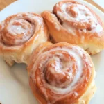 Freshly baked cinnamon rolls with golden swirls, gooey cinnamon filling, and creamy vanilla glaze dripping over the top, served warm.