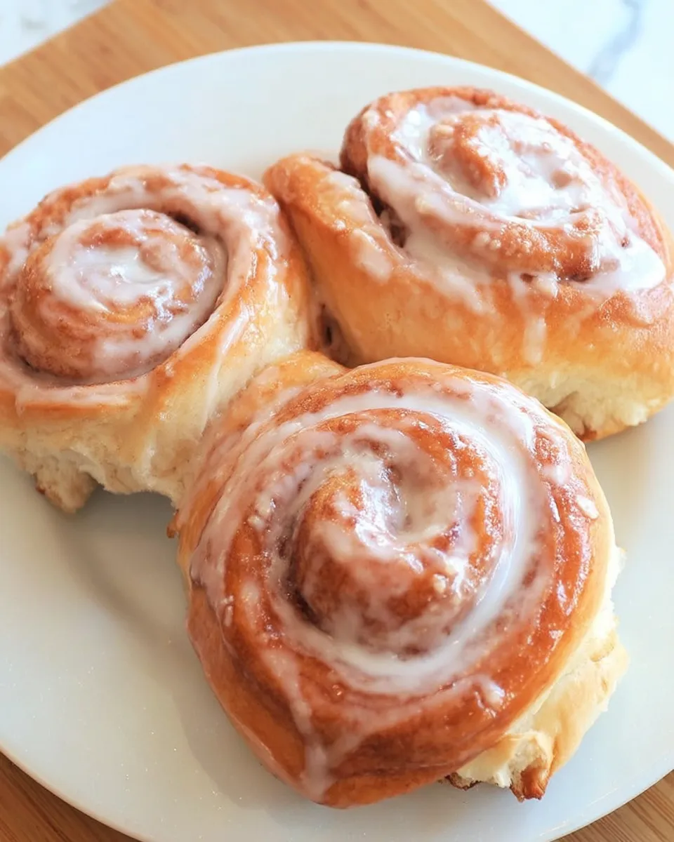 Freshly baked cinnamon rolls with golden swirls, gooey cinnamon filling, and creamy vanilla glaze dripping over the top, served warm.