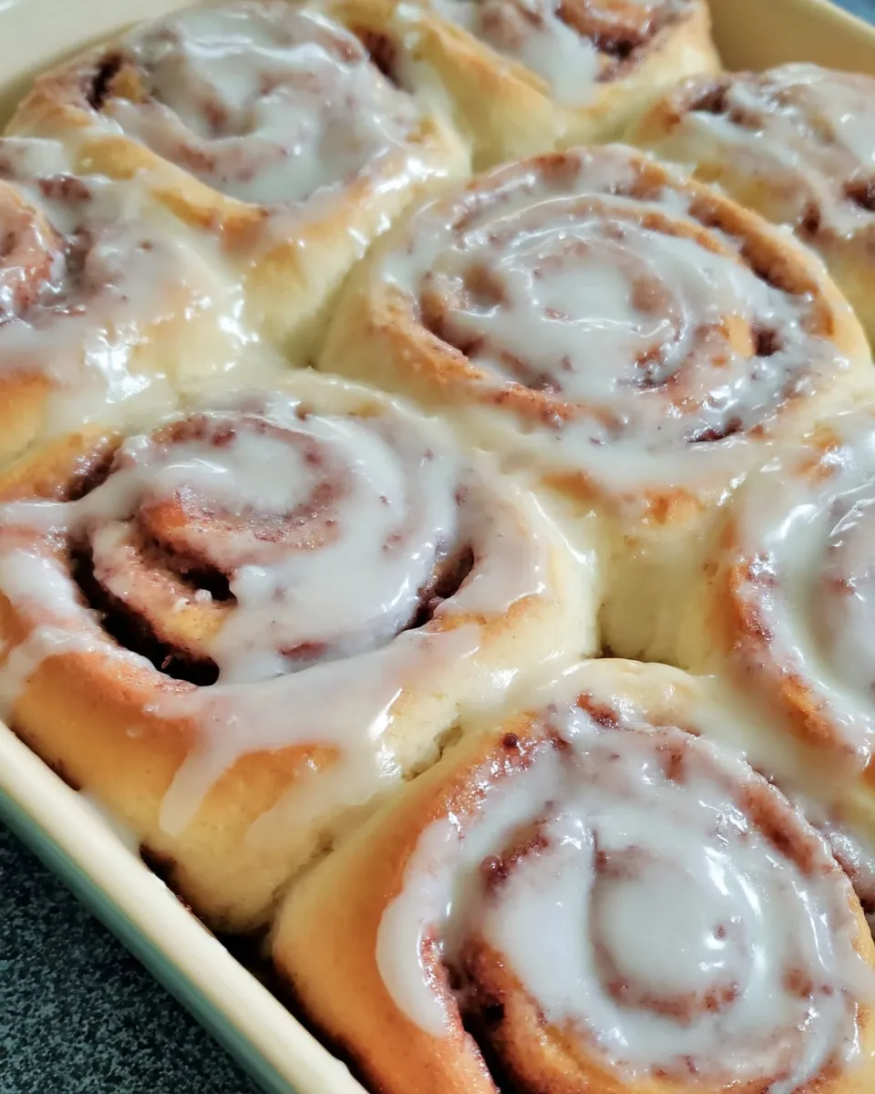 Freshly baked cinnamon rolls with golden swirls, gooey cinnamon filling, and creamy vanilla glaze dripping over the top, served warm.