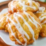 Golden, crispy peach fritters with chunks of fresh peaches, glazed with vanilla icing and stacked on a rustic cooling rack.