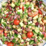 A colorful Double Bean Mediterranean Salad with chickpeas, kidney beans, cucumber, tomatoes, red onion, olives, and fresh herbs tossed in olive oil and lemon dressing.