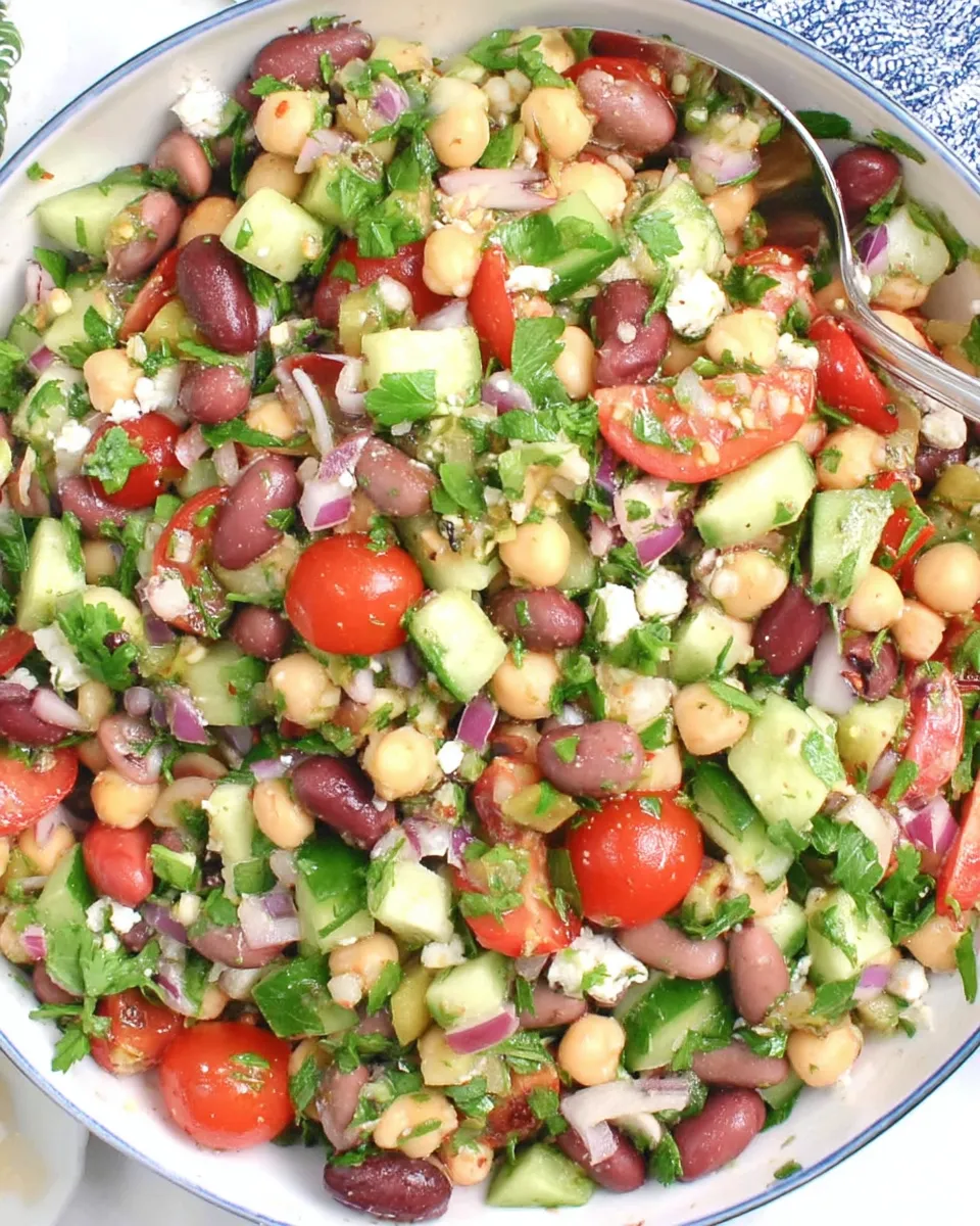 A colorful Double Bean Mediterranean Salad with chickpeas, kidney beans, cucumber, tomatoes, red onion, olives, and fresh herbs tossed in olive oil and lemon dressing.