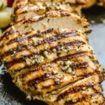 Grilled Greek Marinated Chicken thighs garnished with fresh herbs and lemon wedges on a rustic plate.