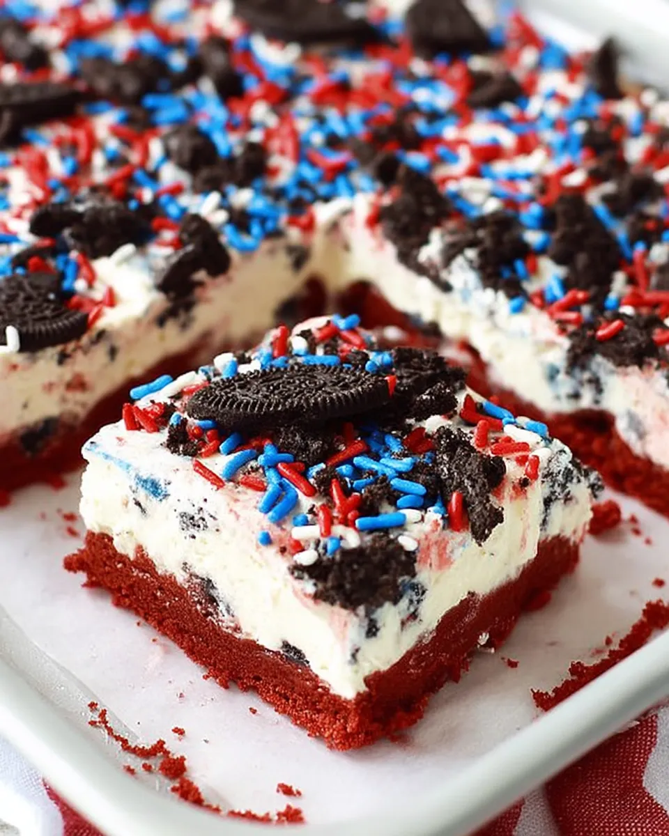Colorful No Bake Fireworks Oreo Cheesecake Bars topped with whipped cream and red, white, and blue sprinkles, layered on a crushed Oreo crust and served on a festive tray.