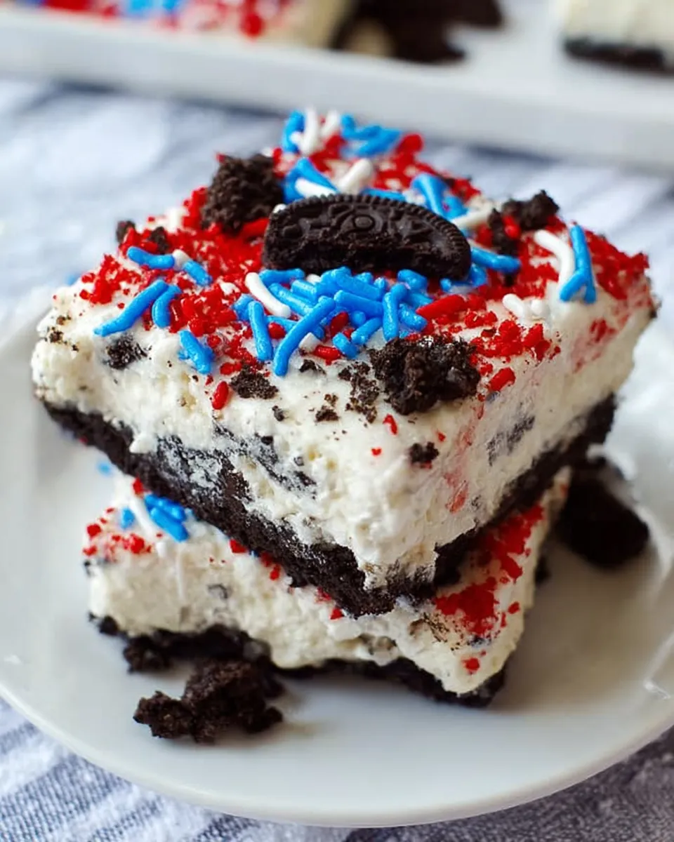 Colorful No Bake Fireworks Oreo Cheesecake Bars topped with whipped cream and red, white, and blue sprinkles, layered on a crushed Oreo crust and served on a festive tray.