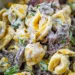 Philly cheesesteak tortellini pasta with melted cheese, peppers, and onions in a skillet