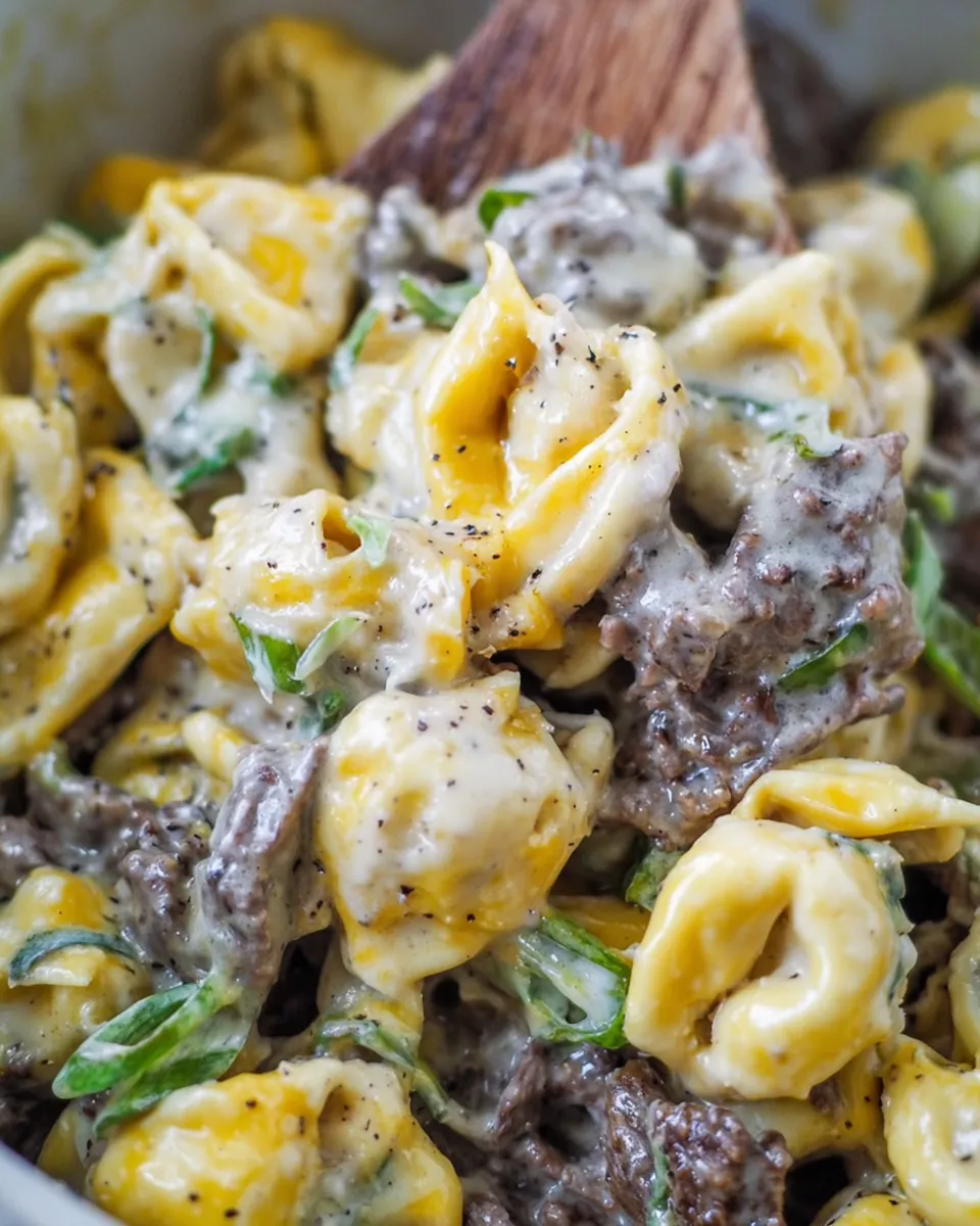 Philly cheesesteak tortellini pasta with melted cheese, peppers, and onions in a skillet