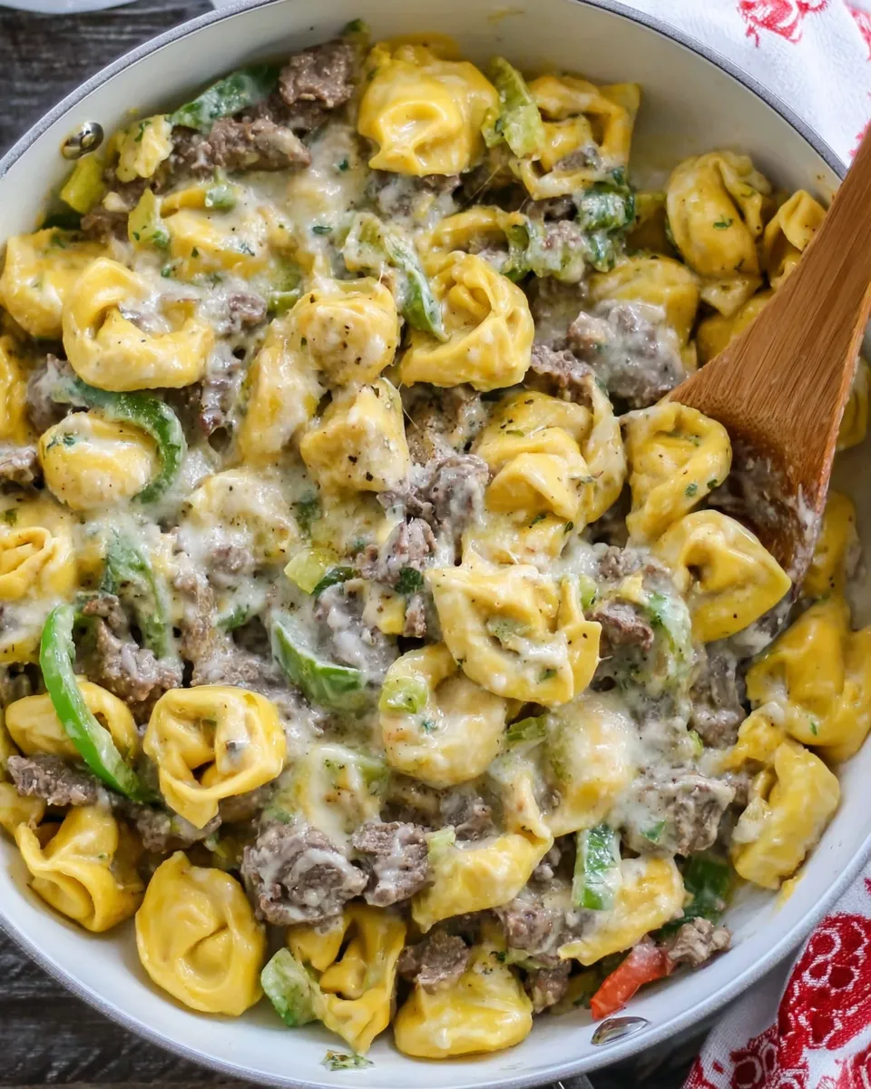 Philly cheesesteak tortellini pasta with melted cheese, peppers, and onions in a skillet