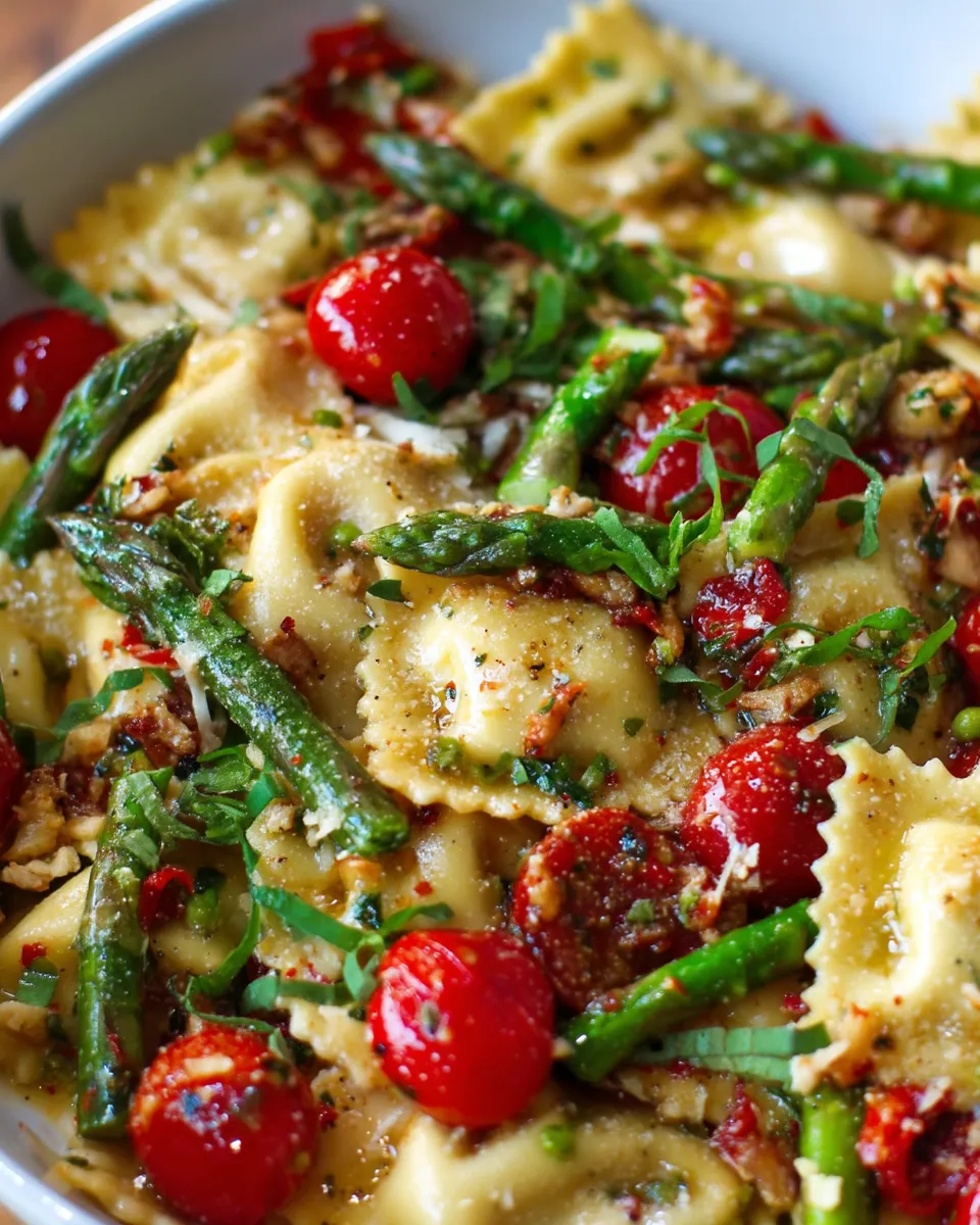 Close-up of cheese ravioli tossed with blistered cherry tomatoes, tender asparagus, fresh herbs, and garlic in a light olive oil sauce.