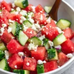 A vibrant summer salad featuring juicy watermelon cubes, crisp cucumber slices, crumbled feta cheese, and fresh mint, served in a white bowl.