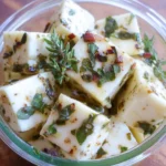 Marinated cheese cubes with herbs and oil in a glass jar
