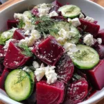 Beet salad with crumbled feta, sliced cucumbers, and fresh dill on a white plate