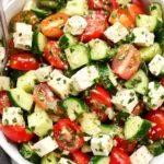 Fresh Greek salad with cucumber, tomato, red onion, olives, and feta cheese in a white bowl