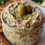 Green olive dip in a bowl garnished with chopped olives and parsley, served with crackers