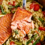 Creamy lemon salmon orzo skillet with fresh herbs and lemon slices in a black pan