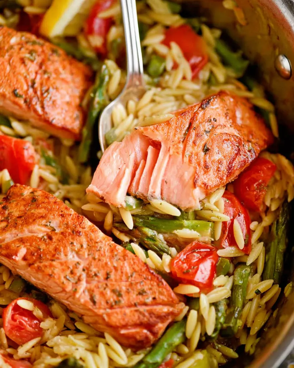 Creamy lemon salmon orzo skillet with fresh herbs and lemon slices in a black pan