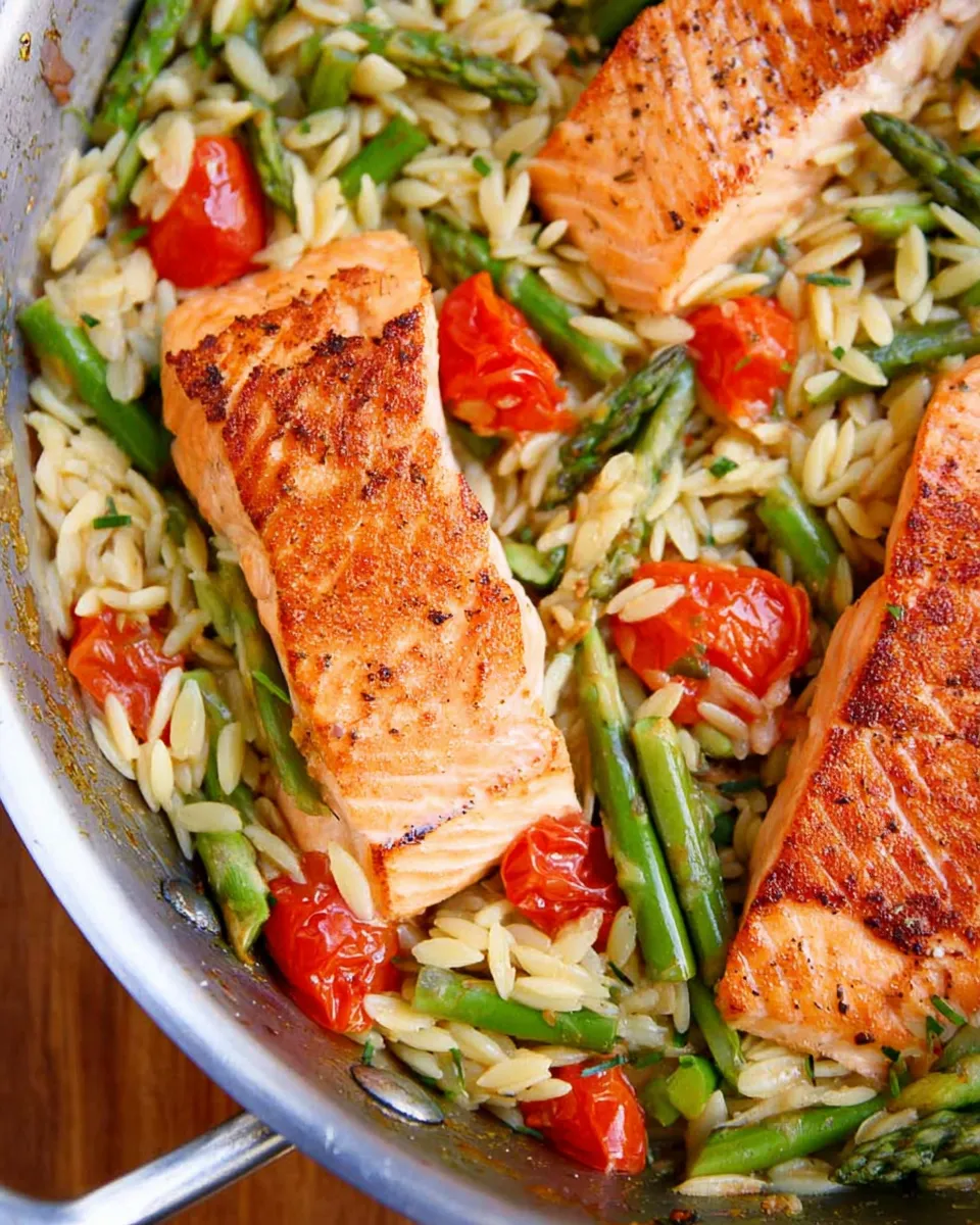 Creamy lemon salmon orzo skillet with fresh herbs and lemon slices in a black pan