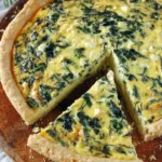Golden spinach and feta quiche slice on a plate with fresh herbs