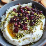 Whipped feta dip topped with honey, chopped pistachios, and cranberries served in a bowl with crackers