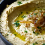 Caramelized onion hummus in a bowl with a swirl of olive oil and herbs