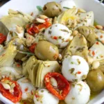 Marinated mozzarella balls, artichokes, and olives in a bowl with herbs