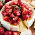 Warm baked brie topped with roasted strawberries on a serving board