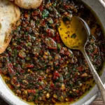 Sun-dried tomato olive oil bread dip in a small bowl with herbs