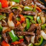 Slow cooker pepper steak with onions served over rice in a bowl.