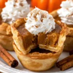 Mini pumpkin pies with whipped cream on top, served on a holiday platter.